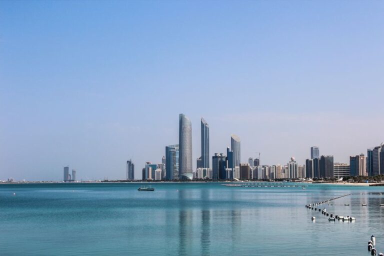 Stunning view of the Abu Dhabi skyline reflecting in the calm Gulf waters on a sunny day.