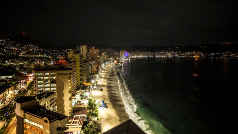 Stunning aerial view of Acapulco's coastline at night with illuminated cityscape and ocean.
