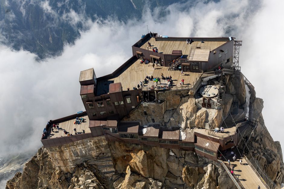 Aerial view of mountain platform with people enjoying scenic views, surrounded by clouds.