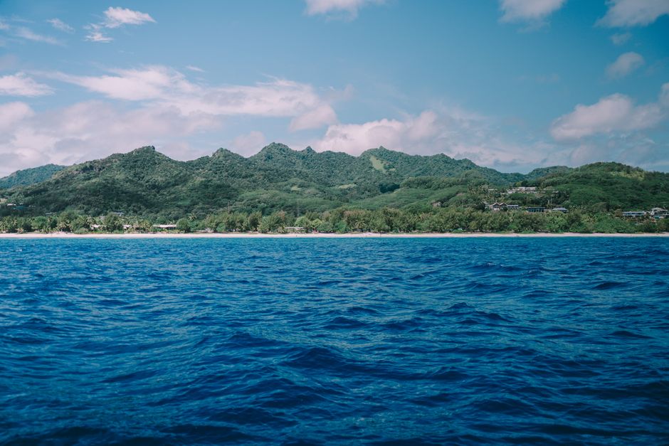 Breathtaking view of lush green island with mountains and clear blue ocean under a bright sky.