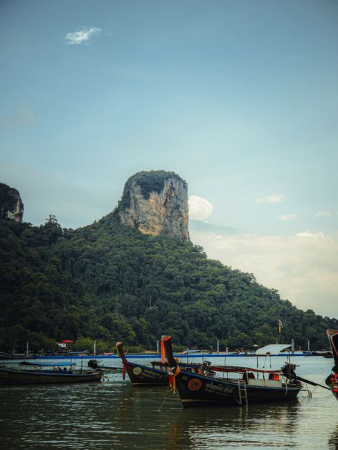 Scenic view of traditional long-tail boats against lush Krabi cliffs, Thailand.