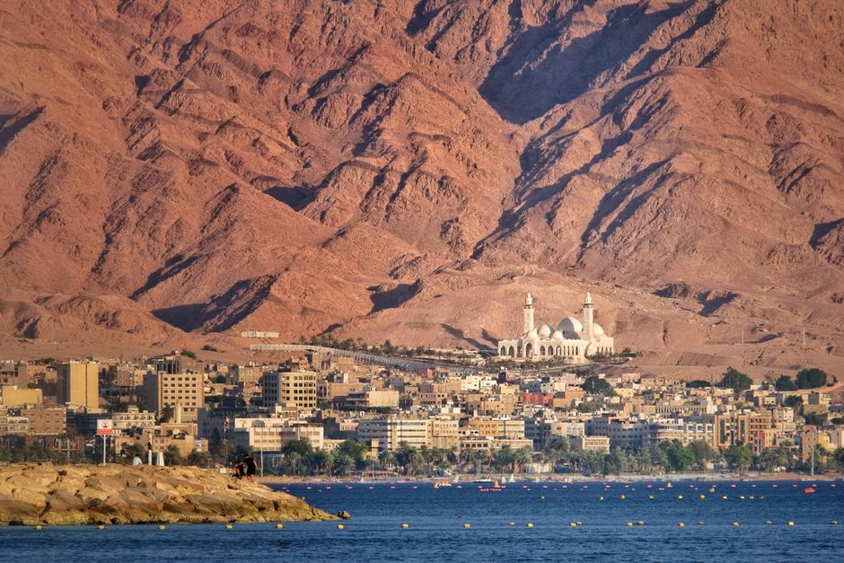 A scenic view of Aqaba city against a dramatic mountain backdrop by the sea.