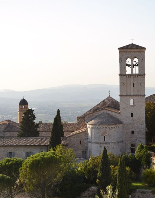 Tranquil view of a historic basilica and landscape in Assisi, Italy, during daylight.