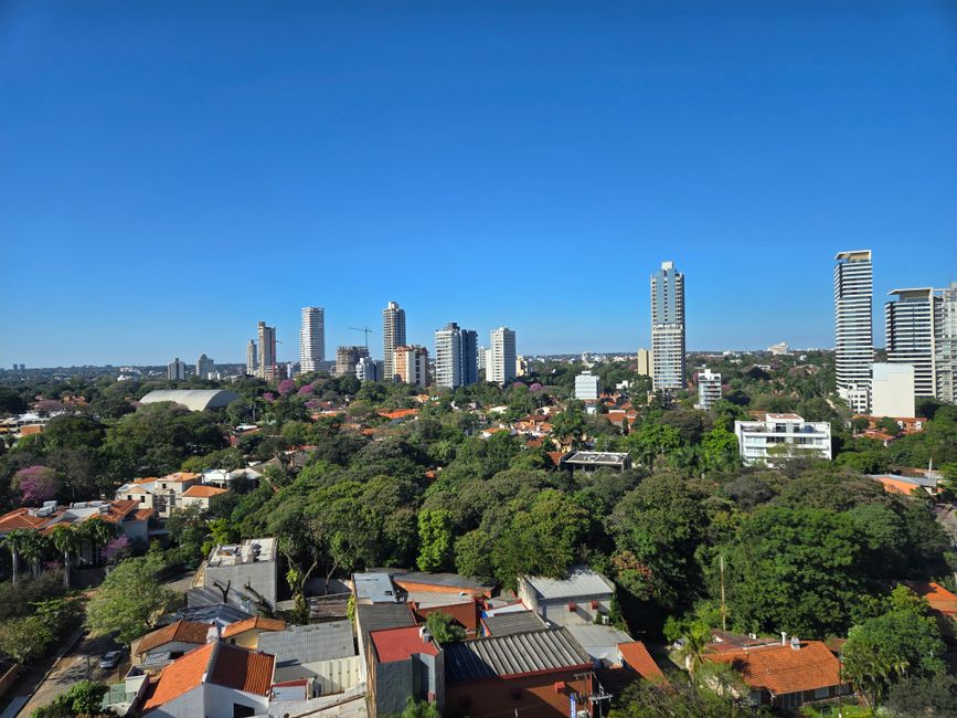 A serene cityscape showcasing a vibrant mix of tall buildings and abundant green spaces under a clear blue sky.