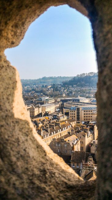 Picturesque view of Bath, England seen through a stone archway, highlighting historic architecture.