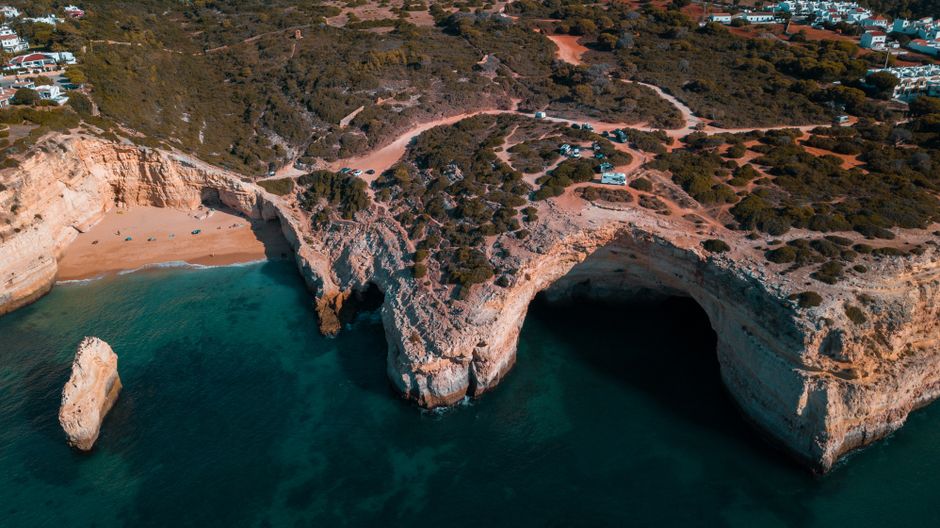 Stunning aerial view of rocky coastal cliffs with clear blue sea and sandy beach in a natural landscape.
