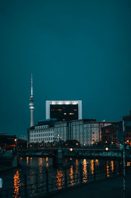 Night view of Berlin's TV Tower reflected in Spree River, showcasing urban architecture.