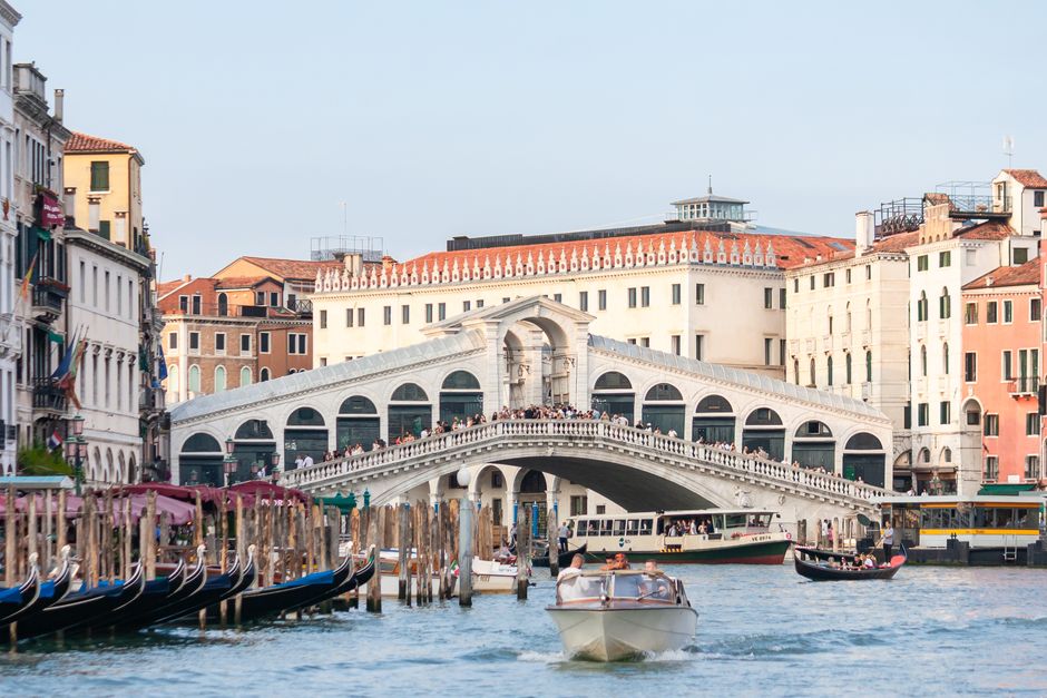 Iconic view of Rialto Bridge with bustling boats on the Grand Canal in Venice, Italy.