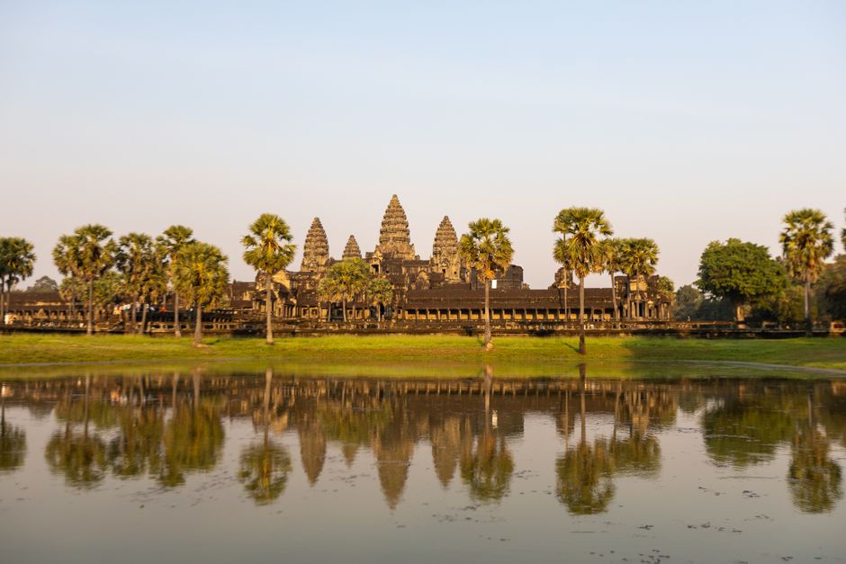 Angkor Wat temple reflecting in water at sunrise, showcasing its historic architecture.