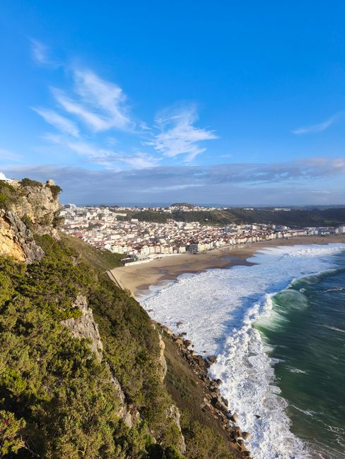 A breathtaking view of the Nazaré coastline, showcasing the beach and Atlantic Ocean under a blue sky.