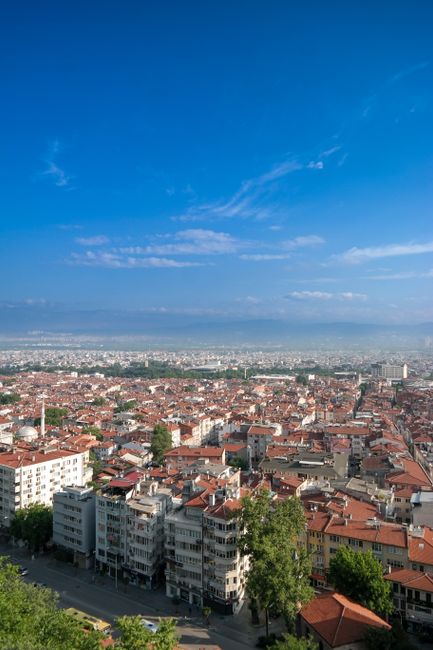 A stunning aerial view of Bursa city, Turkey, showcasing red-tiled roofs under a bright blue sky.