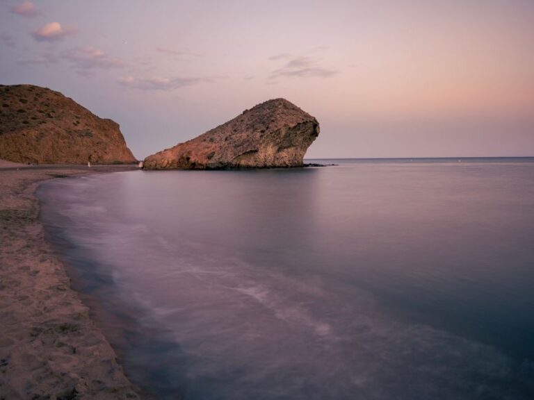 Serene view of a coastal rock formation at dusk in Almería, Spain, with calm seas and a pastel sky.
