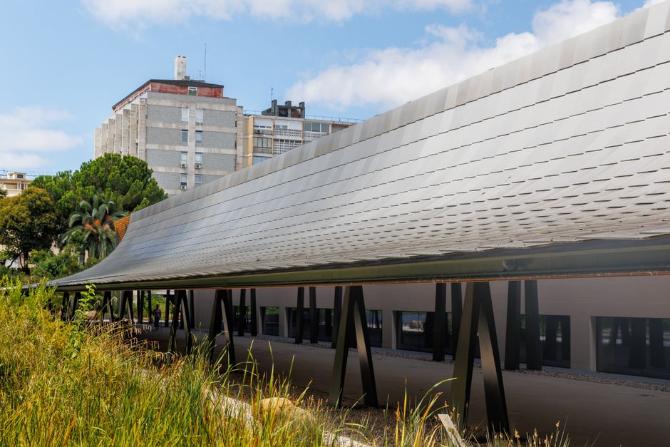 A sleek modern structure with a curved roof amidst urban Lisbon, surrounded by greenery.