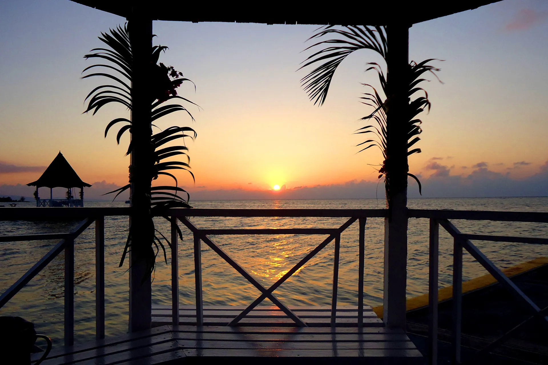Sunset over the Caribbean Sea framed by palms from a seaside gazebo, Jamaica