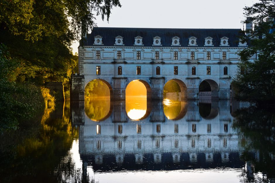 Château de Chenonceau beautifully reflected at sunset, highlighting its arches and elegant architecture.