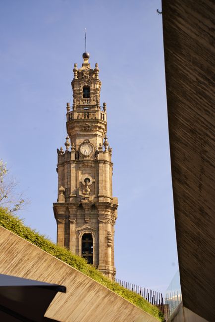 View of the iconic Clérigos Tower in Porto, Portugal, framed by modern architecture against a clear blue sky.