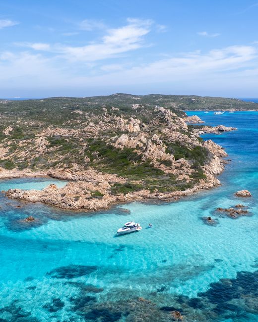 Aerial shot of a boat in stunning turquoise waters near rocky coastline under blue skies.