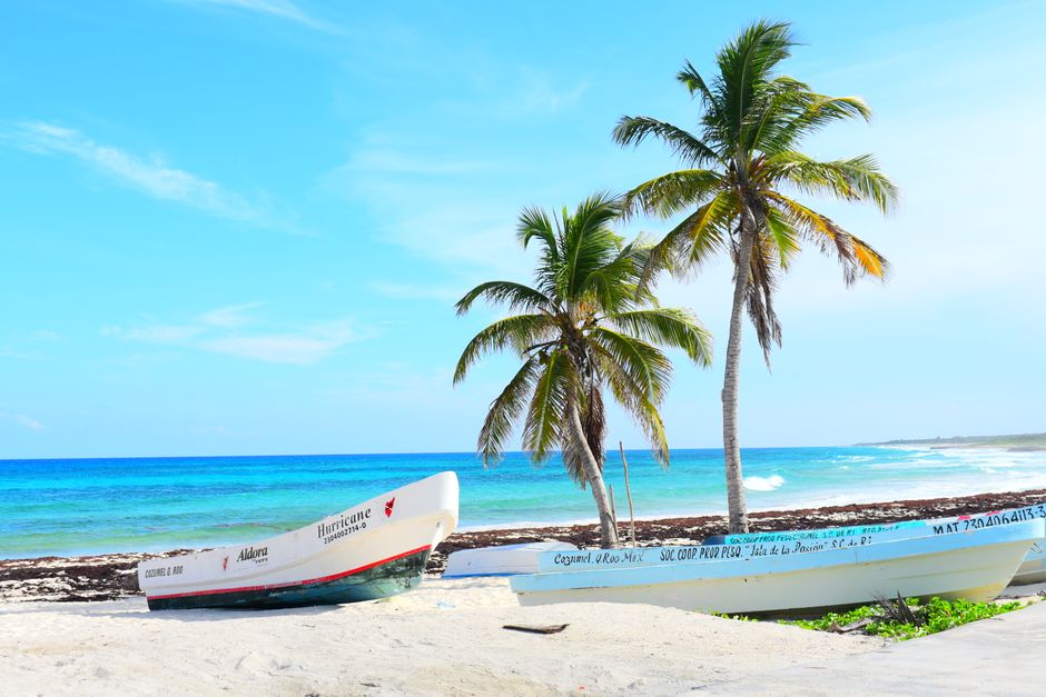 Bright tropical beach featuring boats on the shoreline under clear blue skies and palm trees.