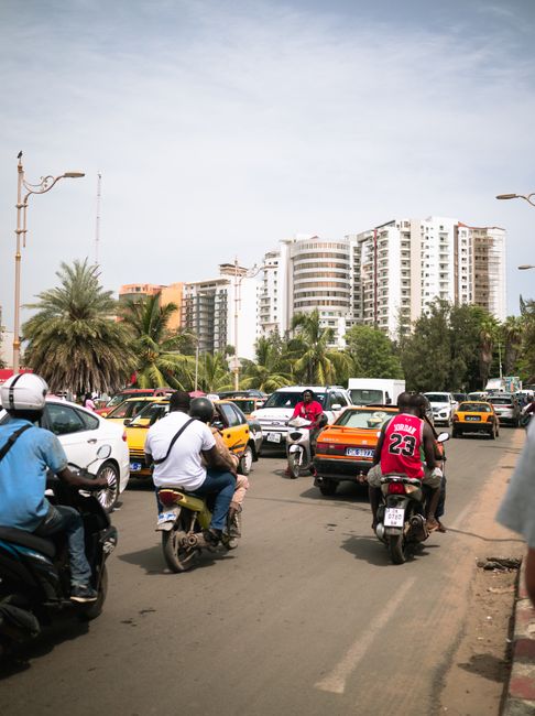 City street in Dakar with motorbikes and cars navigating heavy traffic, showcasing urban life.