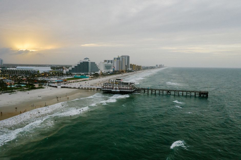 A stunning aerial view of Daytona Beach's pier and coastline at sunset with vibrant ocean waves.