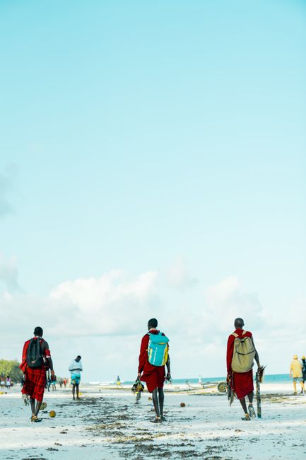 Masai men in traditional attire stroll along Diani Beach, captured in vibrant daylight.