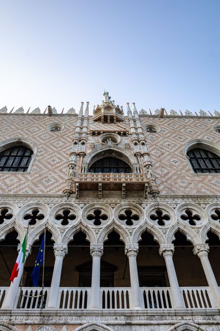Gothic architectural detail of Doge's Palace with Italian and EU flags in Venice.