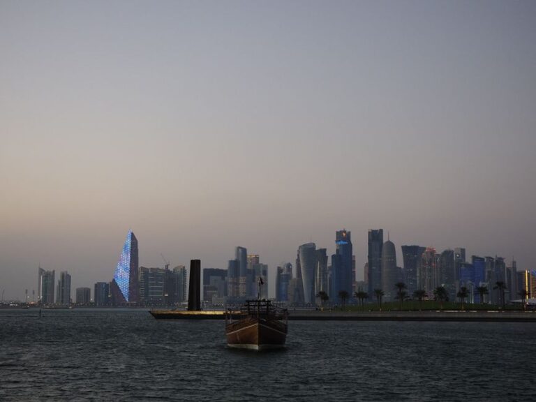 Scenic view of Doha city skyline with traditional dhow boat at dusk along the waterfront.
