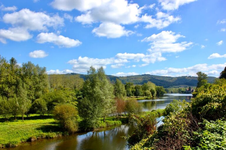 Picturesque landscape of Dordogne River in Beaulieu-sur-Dordogne with lush greenery under blue skies.