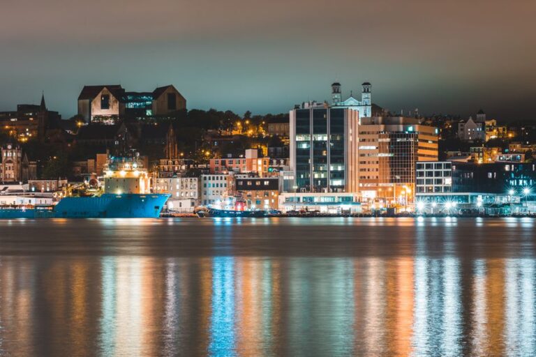 Picturesque cityscape of St John s with harbor and modern and aged buildings located on seashore at night