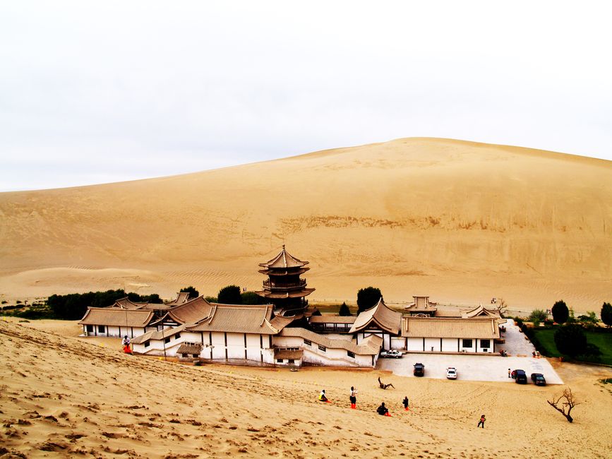 A scenic view of a temple at Echoing-Sand Mountain, Dunhuang, surrounded by desert sand dunes.