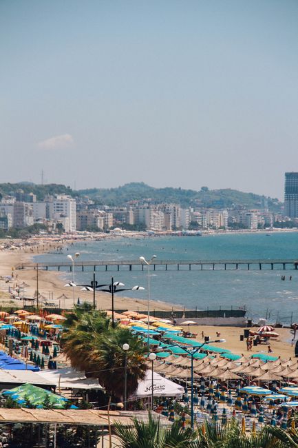A vibrant view of Durrës beach with umbrellas, people, and the city skyline in summer.