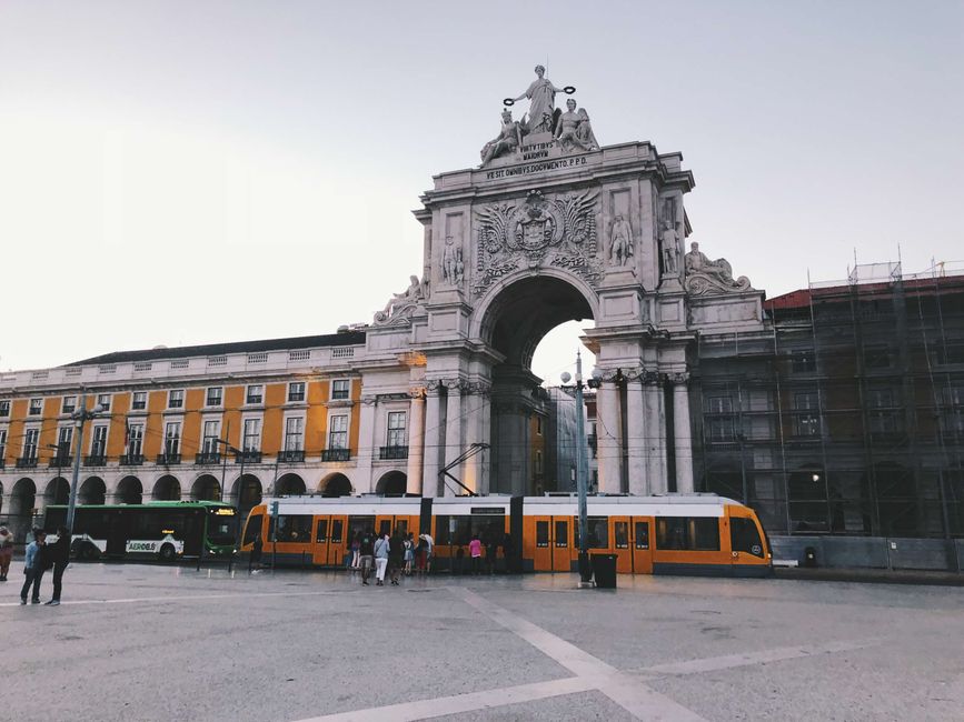 A vibrant Lisbon tram passes in front of the historic Rua Augusta Arch, a notable city landmark.