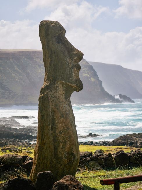 A majestic Moai statue stands by the rugged coast of Easter Island, Chile, against a backdrop of waves and cliffs.