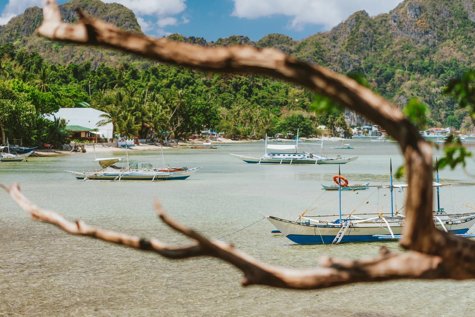 Fishing boats moored in a lagoon with a sandy beach and rocky cliffs, El Nido, Philippines