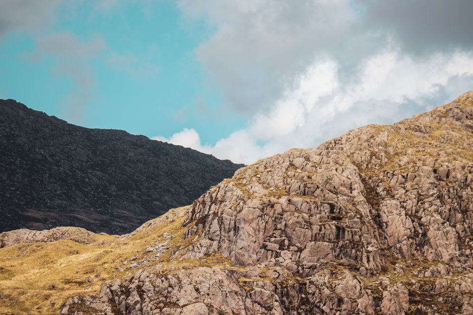 Explore the rugged beauty of rocky cliffs and mountain ranges in Wales under a clear blue sky.