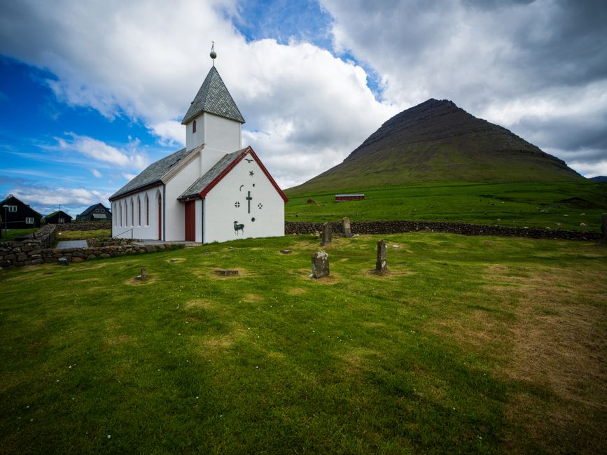 A tranquil scene of a Faroese church set against a lush mountainous backdrop under a vibrant sky.