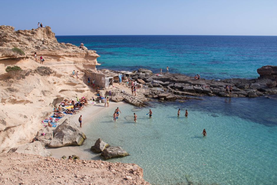 Stunning coastline photo capturing beachgoers at a rocky cove in Illes Balears, Spain.