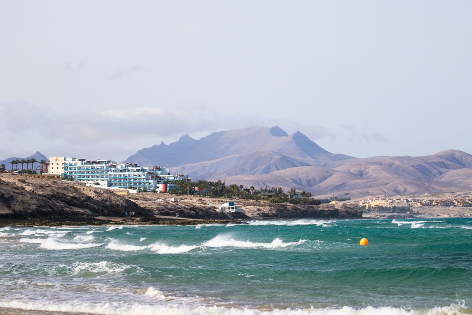 Scenic view of Fuerteventura coastline with waves and mountains in the background.