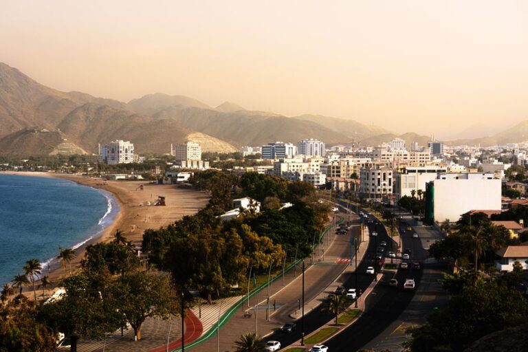 Aerial view of Khor Fakkan's scenic coastline, urban skyline, and mountains at sunset.