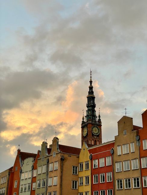 A picturesque view of historic buildings and a clock tower in Gdańsk, Poland, at sunset.
