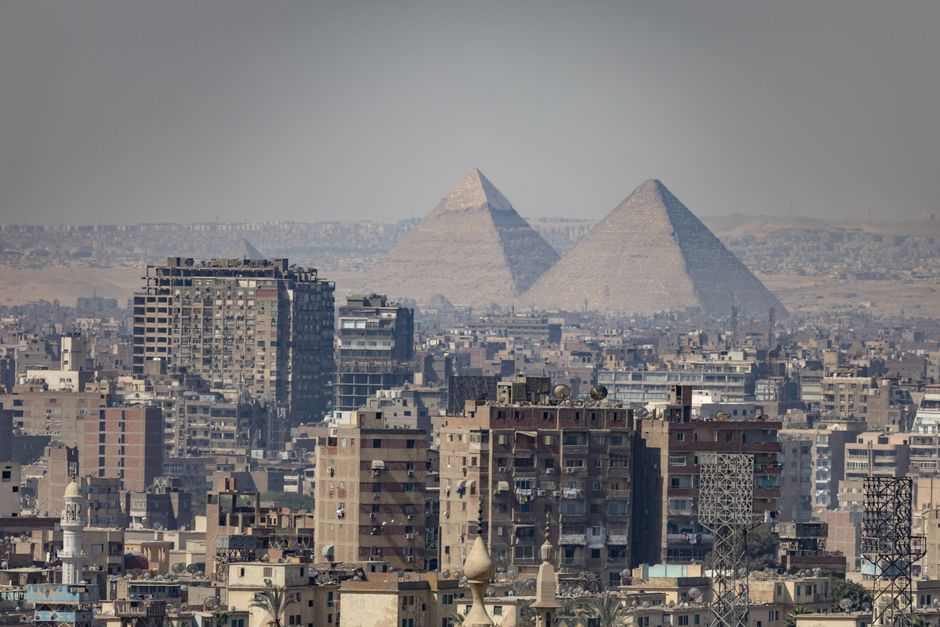 Aerial view of Cairo, Egypt, showcasing urban buildings with the iconic Pyramids of Giza in the background.
