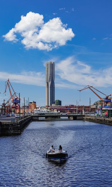 A serene day at Göteborg harbor with a boat on the water and Karlatornet skyscraper in the distance.