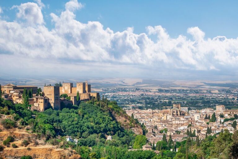 A scenic view of the historic Alhambra in Granada, Spain, surrounded by lush greenery and an expansive cityscape.