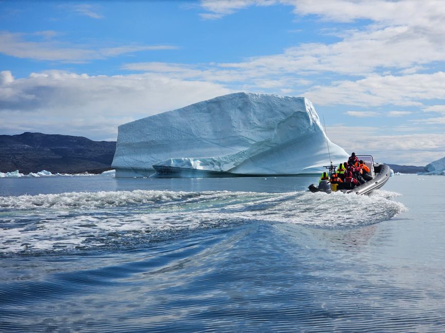 Tourists enjoy a thrilling boat ride near a majestic iceberg in Greenland under a clear sky.