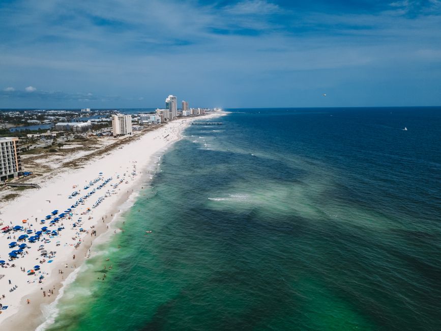 Aerial shot of a bustling beachfront with green waters and tall buildings under a clear sky.