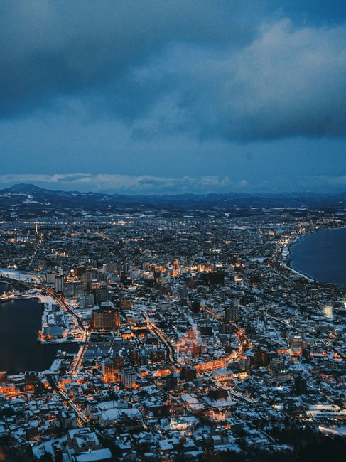 Stunning aerial view of Hakodate at night, showcasing a winter landscape and illuminated city lights.