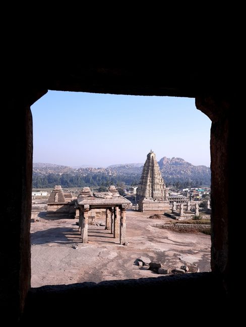 View of Virupaksha Temple in Hampi framed by ancient ruins, showcasing architectural beauty against clear sky.