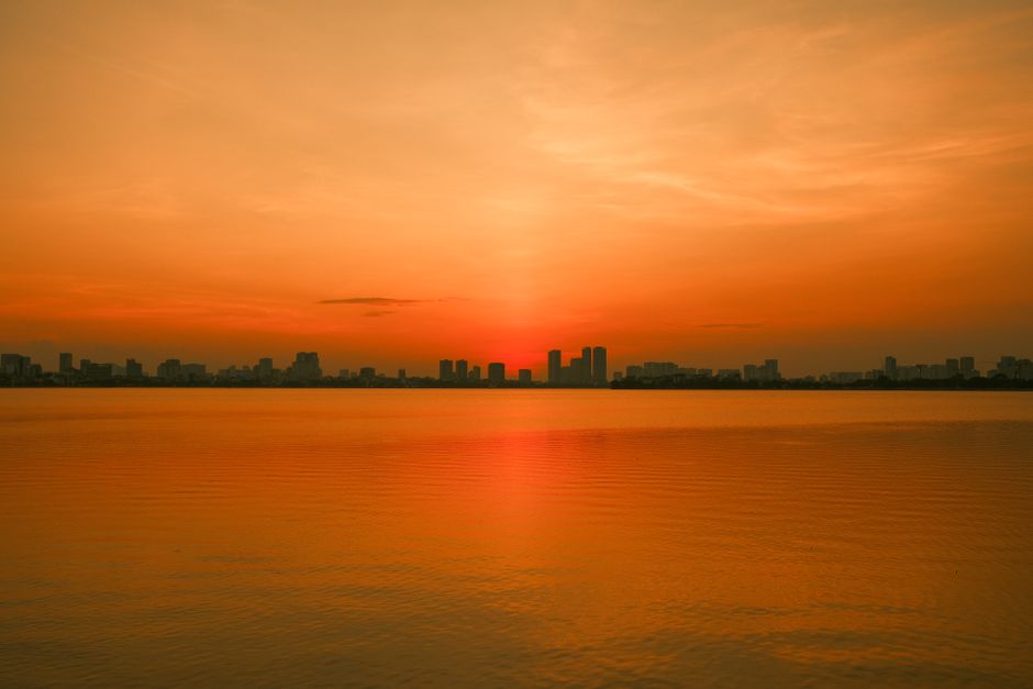 A vivid sunset casts a golden hue over the serene waters of Hanoi, Vietnam.