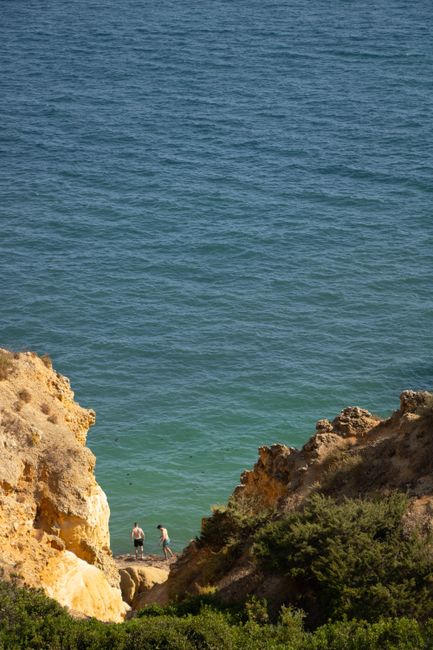 Scenic view of Algarve's sea cliffs and the Atlantic Ocean with two people exploring the beach.