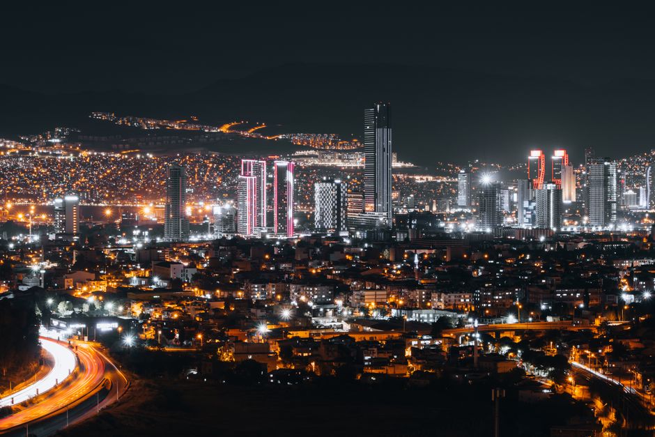 Vibrant nighttime cityscape of İzmir, Türkiye featuring illuminated skyscrapers and urban lights.